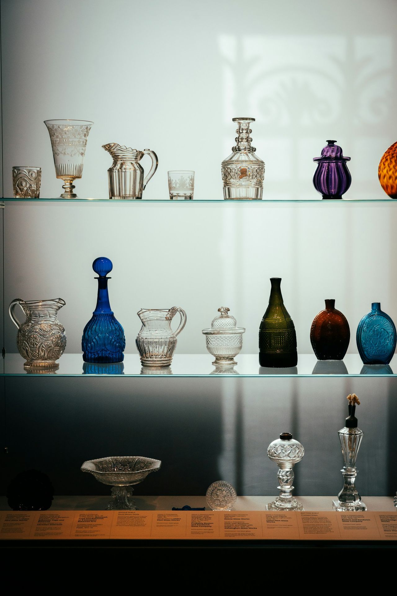 Collection of antique glass and metal vessels on shelves.
